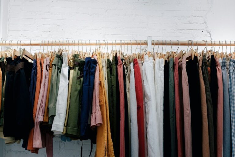 clothes rack with a selection of colored pants and shorts in front of a white painted brick wall